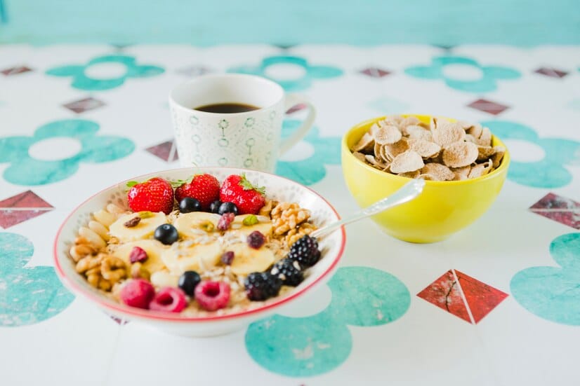 A healthy breakfast setup featuring a bowl of oatmeal topped with fresh berries, banana slices, nuts, and seeds, accompanied by a cup of coffee and a bowl of cereal.