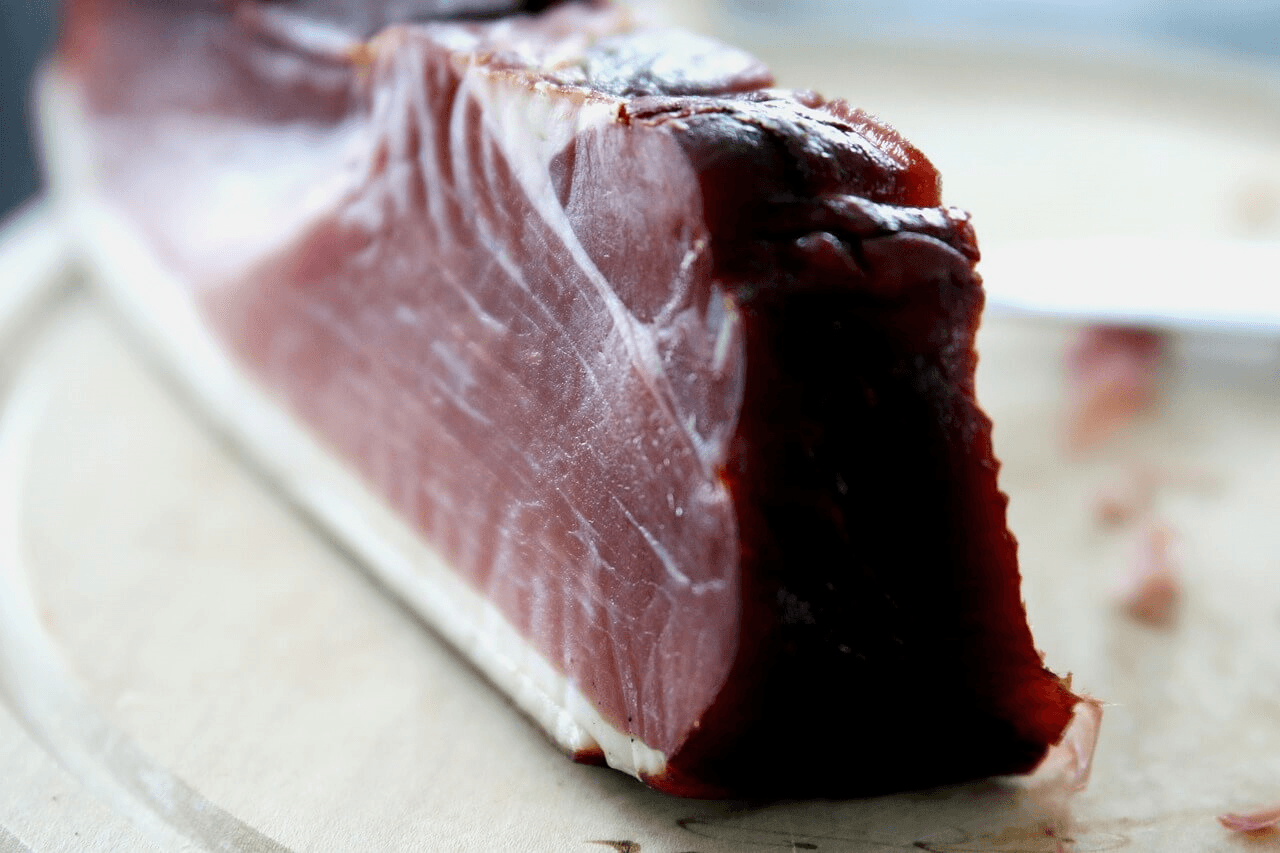 Close-up of a thick slice of cured beef bacon with a rich, smoky texture on a wooden cutting board.