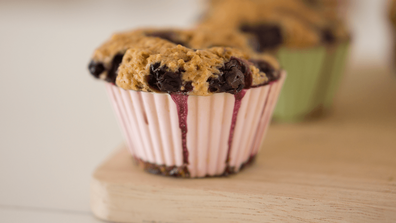 Close-up of a freshly baked blueberry muffin in a pink wrapper, with juicy blueberries and a golden-brown top."