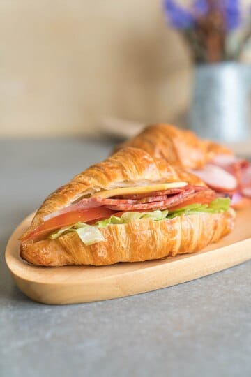 Freshly prepared ham and cheese croissant with lettuce and tomato on a wooden platter