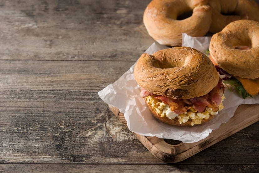 Freshly made bagel sandwich filled with scrambled eggs, crispy bacon, and creamy cheese on a rustic wooden surface