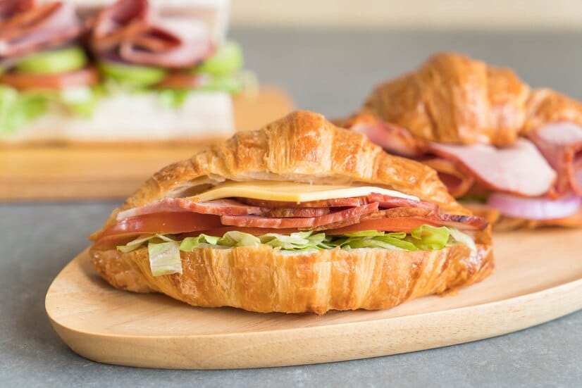 Delicious ham and cheese croissant sandwich with fresh lettuce on a wooden plate, perfect for breakfast or lunch.