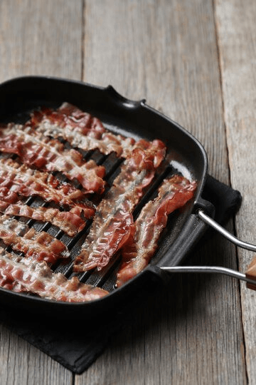 Strips of crispy beef bacon cooking on a black grill pan placed on a rustic wooden table